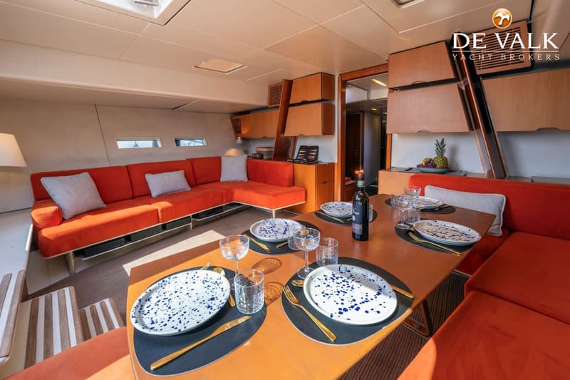 Een interieur van een boot met een oranje bank, een houten tafel met servies en een fles wijn. — Wally 88