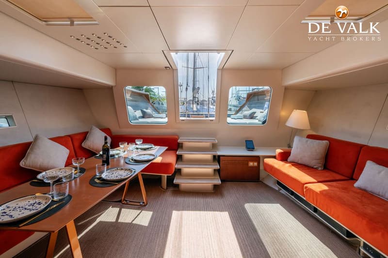 Een interieur van een boot met een eettafel, twee oranje banken, ramen en een dakraam. — Wally 88