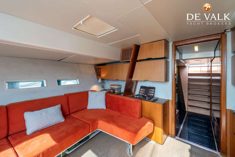 De foto toont een interieur van een boot met een oranje hoekbank, houten kasten en een trap naar beneden. — Wally 88