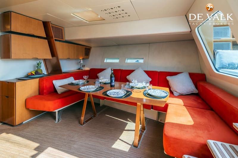 Een interieur van een boot met een houten tafel, rode banken, kussens, servies en een fles wijn. — Wally 88