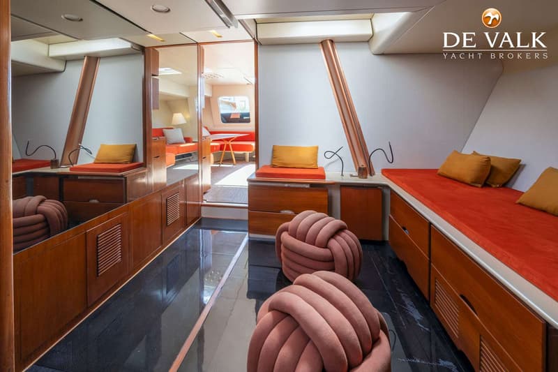 Een interieur van een boot met een glanzende donkere vloer, houten kasten en oranje kussens, met een doorgang naar een…