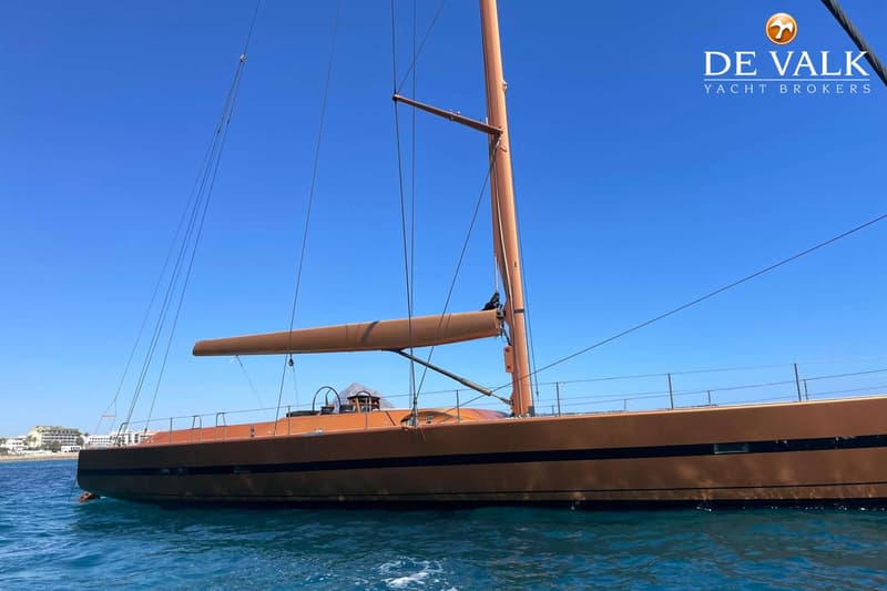 Een zeilboot met een koperkleurige romp en mast ligt in helderblauw water onder een strakblauwe lucht. — Wally 88