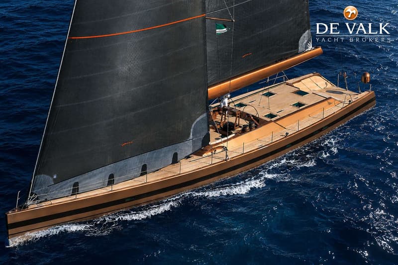 Een zeilboot met een goudkleurige romp en een zwart zeil vaart over een blauwe zee. — Wally 88