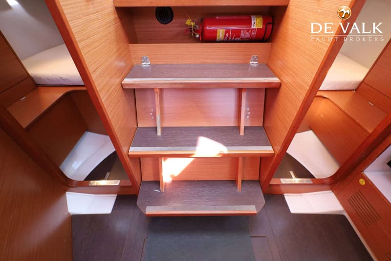 Een houten kajuitinterieur met twee treden, een brandblusser en twee slaapplaatsen aan weerszijden.
