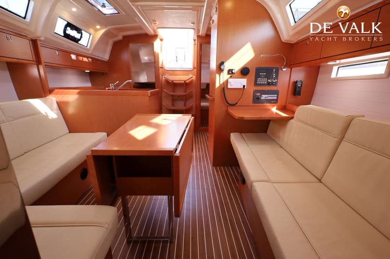 De foto toont het interieur van een boot met houten wanden en vloer, een tafel, banken en een kombuis. — Bavaria 37 Cruiser