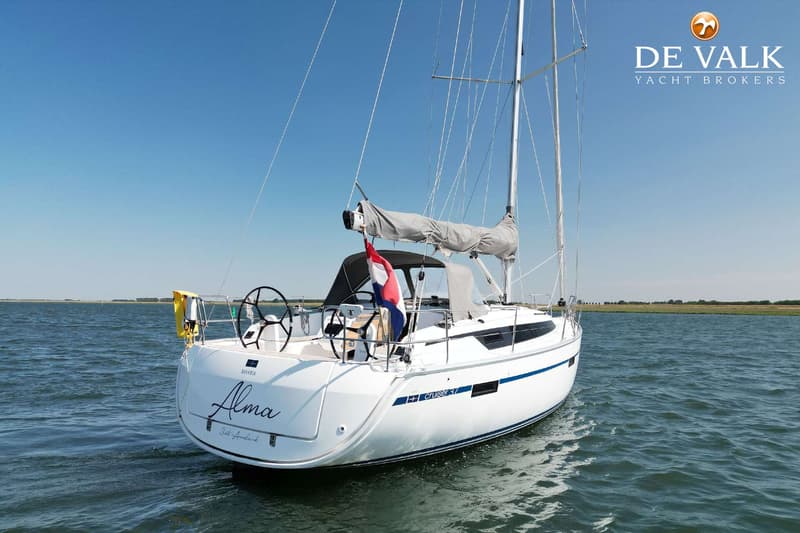 Een witte zeilboot met de naam "Alma" en "Cruiser 37" op de romp, vaart op open water onder een heldere blauwe lucht.
