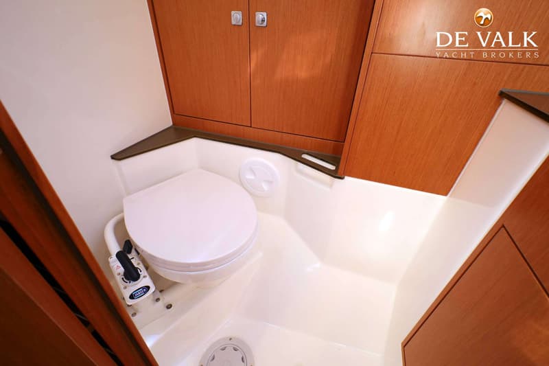 Een witte scheepstoilet met een Jabsco pompmechanisme is zichtbaar in een badkamer met houten kasten.