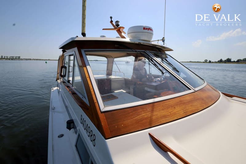 Een witte motorboot met houten accenten vaart op helder water onder een blauwe lucht. — Storebro Royal Cruiser 31 Baltic