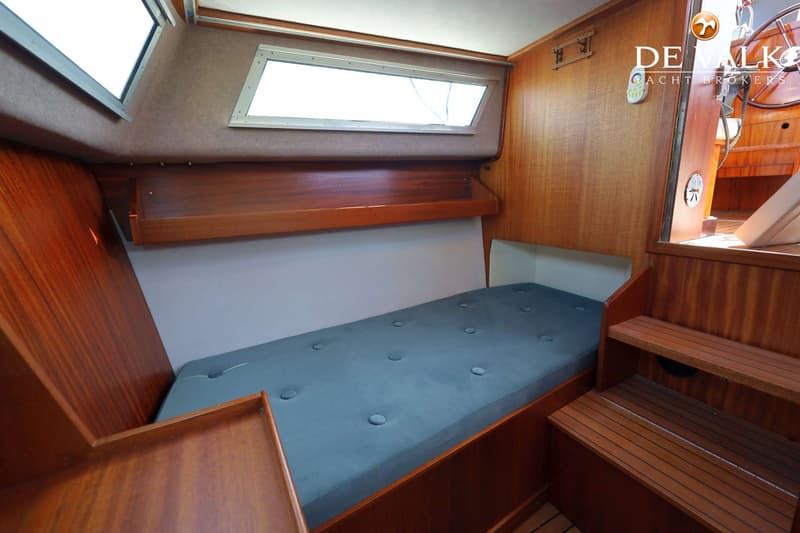 De foto toont een kajuit met een bed met blauwe bekleding, houten wanden en een raam. — Storebro Royal Cruiser 31 Baltic