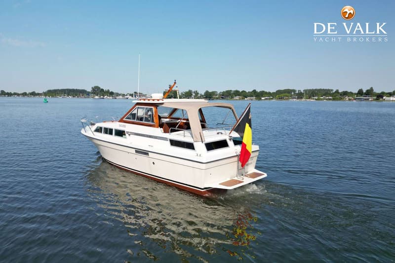 Een witte motorboot met een bruine streep en een Belgische vlag vaart over rustig water. — Storebro Royal Cruiser 31 Baltic