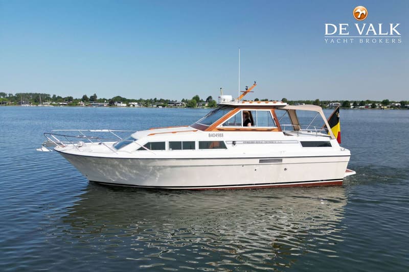 Een witte motorboot met houten details vaart op rustig water onder een heldere blauwe lucht.