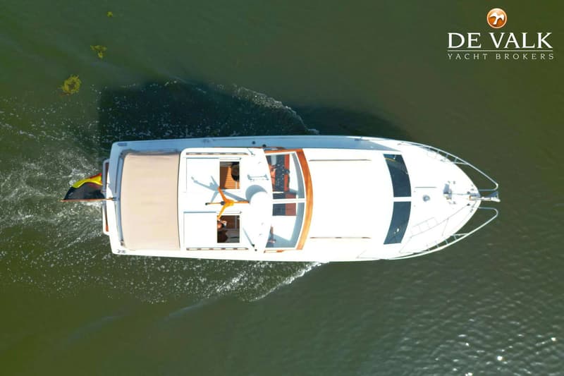 Een witte motorboot met een beige afdekzeil en een Belgische vlag vaart op groen water. — Storebro Royal Cruiser 31 Baltic