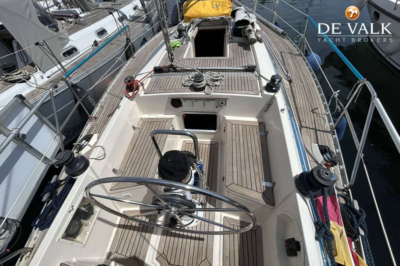 De foto toont het dek van een zeilboot met een stuurwiel, teakhouten dek en een open kajuitingang. — Maestro 35