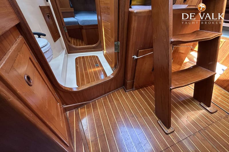 De foto toont een houten interieur van een boot met een trapje, een toilet en een bed met blauwe kussens. — Maestro 35