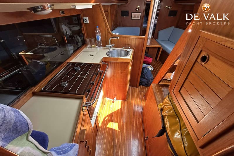 De foto toont een houten interieur van een boot met een kombuis, inclusief een fornuis, spoelbak en opbergruimte.
