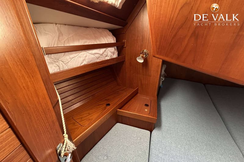 De foto toont een kajuit met houten wanden, een bed met wit dekbed, een lampje en grijze kussens. — Maestro 35