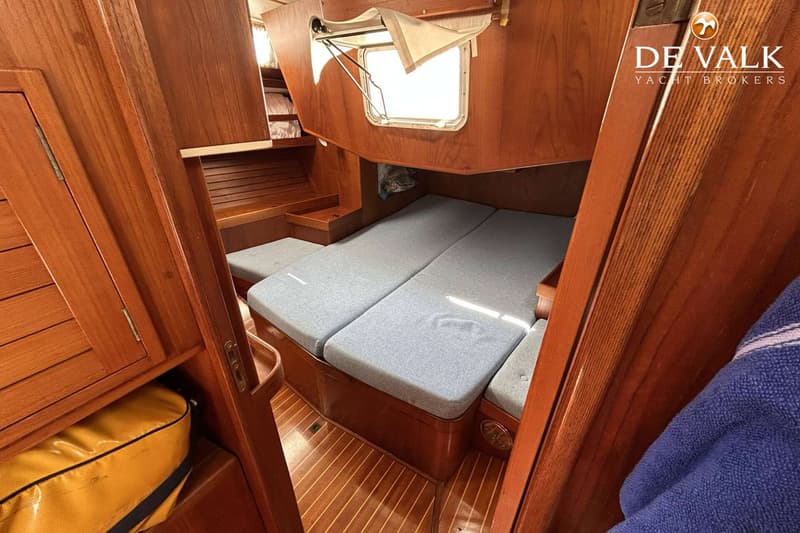 Een interieur van een boot met houten wanden en vloer, een bed met grijze kussens en een open raam. — Maestro 35