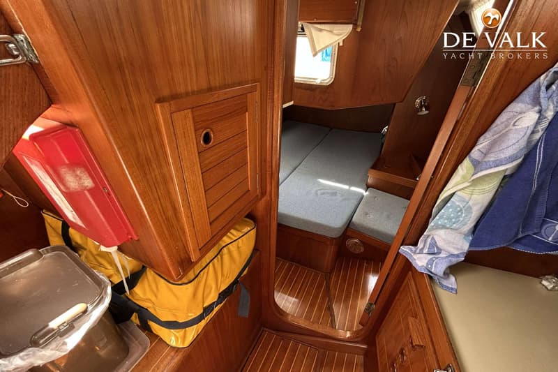 De foto toont een houten interieur van een boot met een kajuit, een bed met grijze kussens en een raam. — Maestro 35