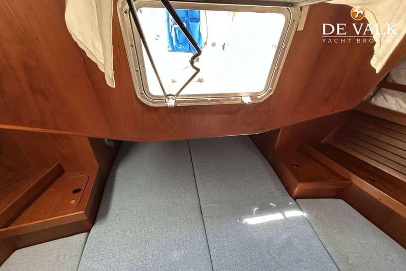Een interieurfoto van een boot met een bed met grijze kussens, houten wanden en een open dakluik. — Maestro 35