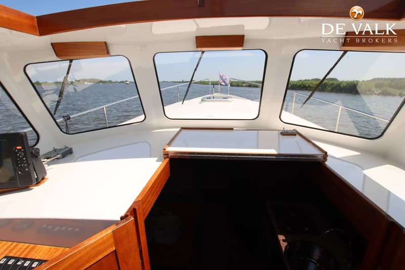 De foto toont het interieur van een boot met uitzicht door de voorruit op water en een Friese vlag.