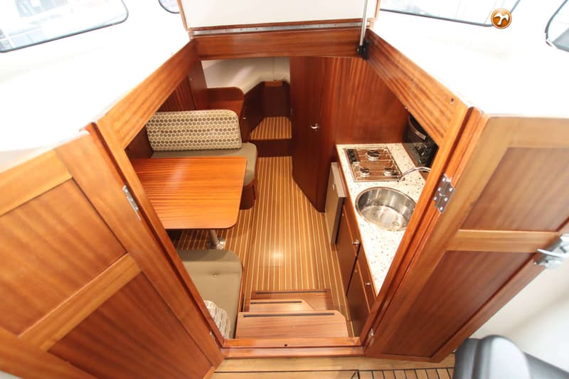 De foto toont het interieur van een boot met een kombuis, zithoek en een trap naar beneden. — Langenberg Vlet 10.25 Cabrio