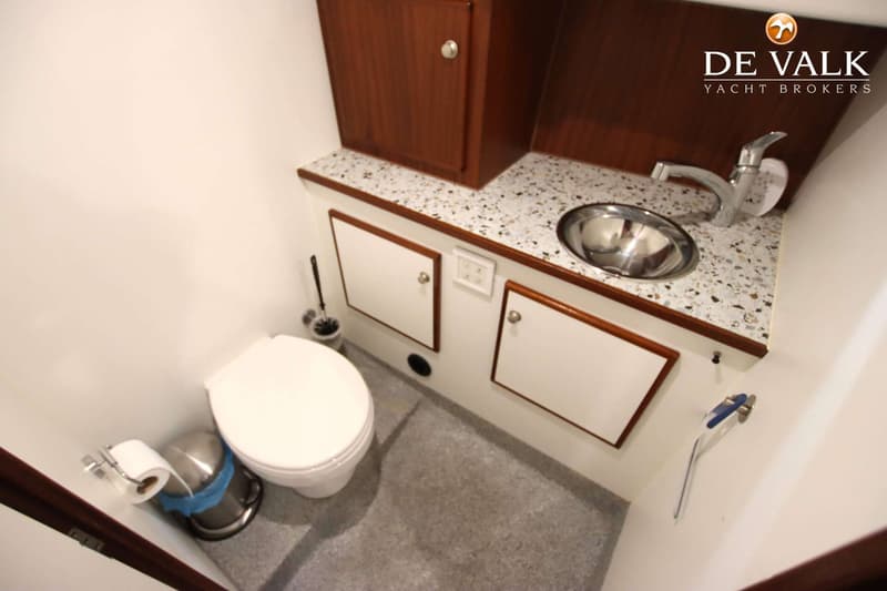 Een badkamer met een wit toilet, een wastafel met kraan, een prullenbak, een toiletborstel en opbergkastjes.