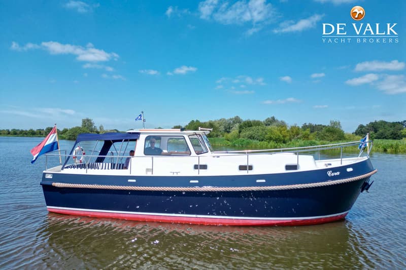 Een blauw-witte motorboot met rode onderkant vaart op een waterweg met bomen op de achtergrond.