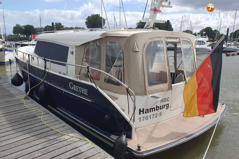 Een donkerblauwe boot met de naam "GRETHE" en "Hamburg 176172-S" op de spiegel, ligt afgemeerd aan een houten steiger.