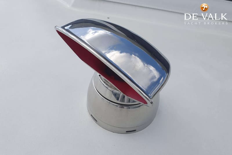 Een close-up van een glimmend metalen ventilatierooster met rode binnenkant op een wit oppervlak.