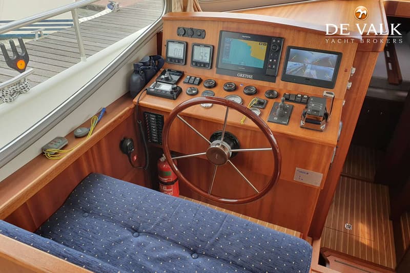 Een houten stuurwiel en een dashboard met diverse meters, schermen en bedieningselementen zijn zichtbaar.