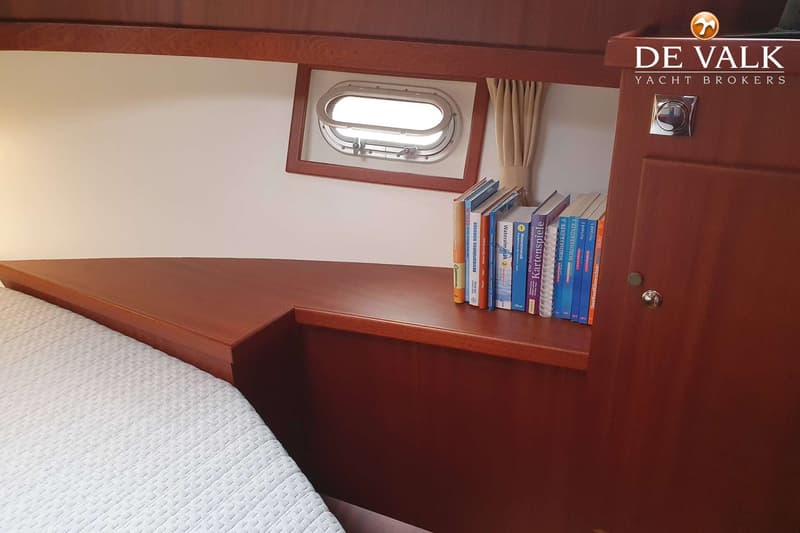 Een kajuit met een bed, een patrijspoort met gordijn, een boekenplank met boeken en een kast. — Brandsma Noordzeekotter 38