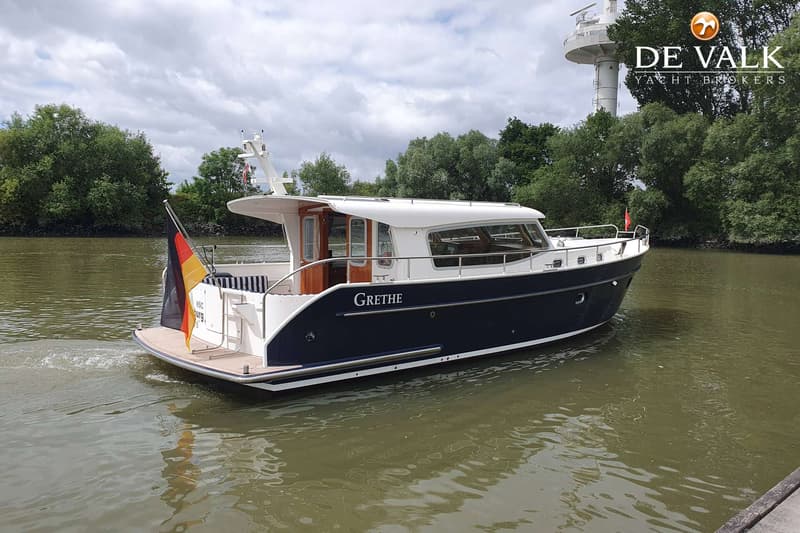 Een blauw-witte motorboot met de naam "GRETHE" vaart op een rivier met een Duitse vlag aan de achtersteven.