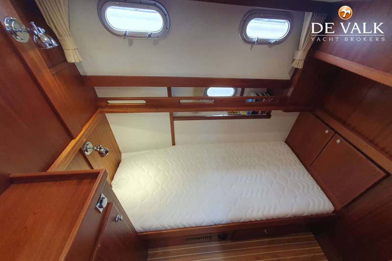 Een kajuit met een bed, twee patrijspoorten, houten lambrisering en een boekenplank. — Brandsma Noordzeekotter 38