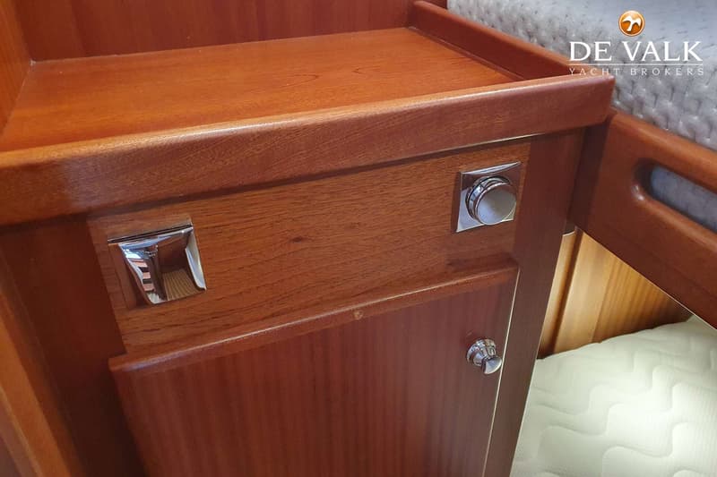 Een detailfoto van een houten kastje met twee chromen handgrepen en een draaiknop, naast een wit matras.