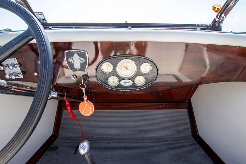 Een close-up van een stuurwiel, dashboard met meters en een thruster-bediening in een boot.
