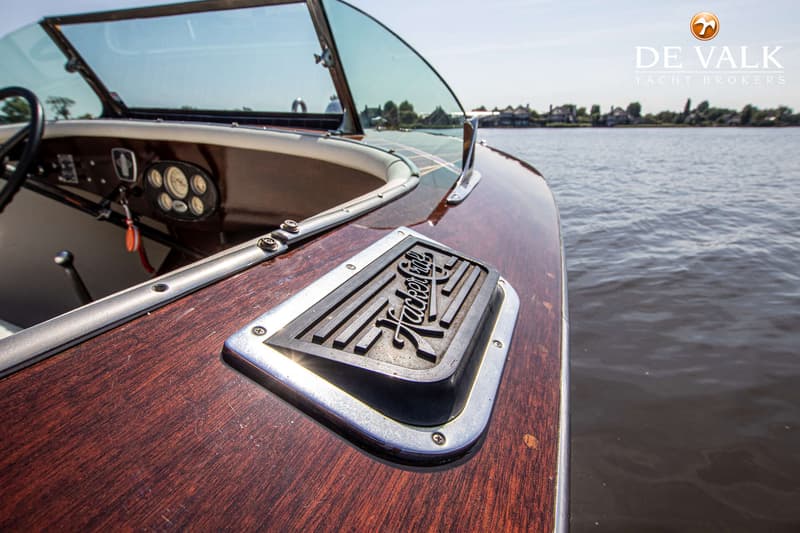 Een close-up van een houten boot met een "Hacker-Craft" logo, een voorruit en een dashboard met meters.