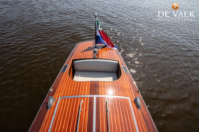 Een bovenaanzicht van de achtersteven van een houten boot met een Nederlandse vlag en een zitgedeelte.
