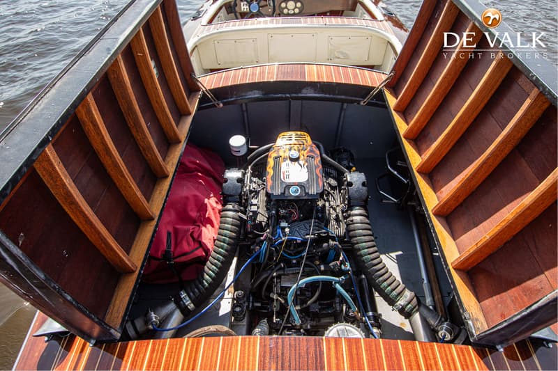 De foto toont een open motorruimte van een boot met een motor met vlammenprint en diverse slangen en kabels.