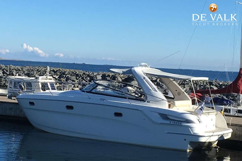 Een witte motorboot met de registratie "S 19868" ligt aangemeerd in een haven met een rotsachtige kustlijn op de achtergrond.