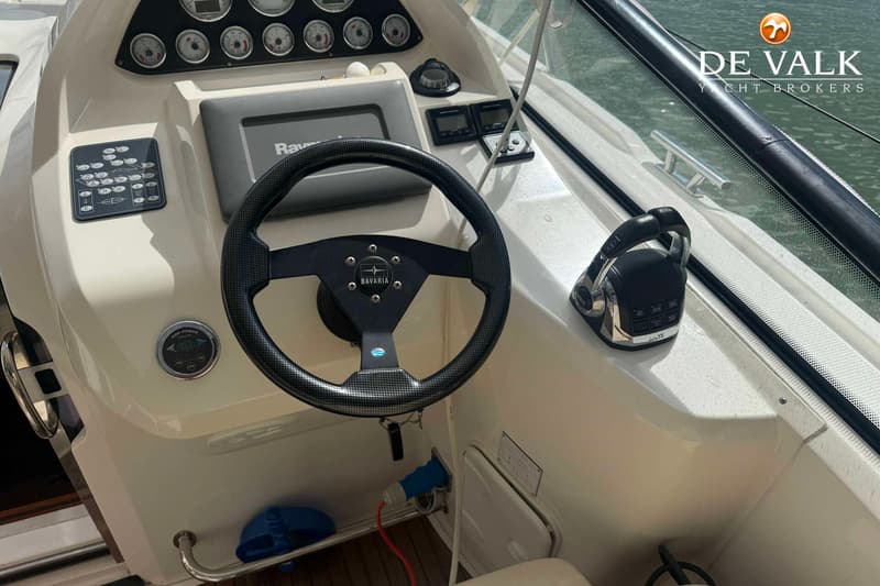 Een stuurwiel met "Bavaria" logo, diverse meters, een Raymarine scherm en een gashendel zijn zichtbaar.