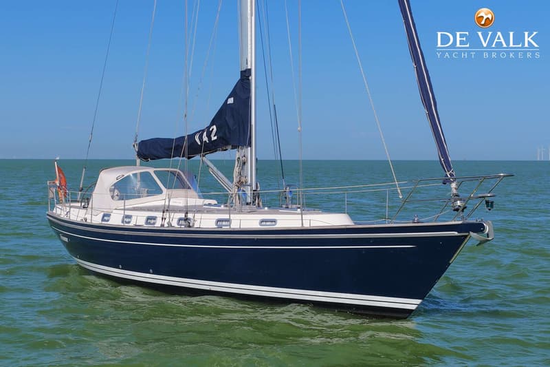 Een donkerblauwe zeilboot met een witte opbouw en een beige buiskap drijft op groen water onder een helderblauwe lucht.