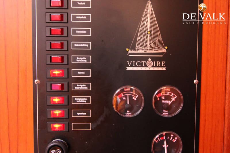 Een zwart bedieningspaneel met rode schakelaars, meters en de tekst "VICTOIRE" en "DE VALK YACHT BROKERS".