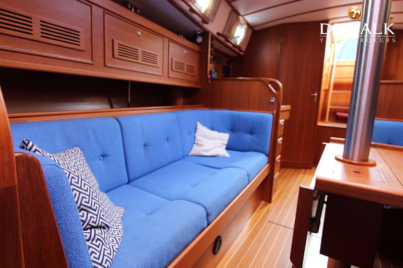 Een interieur van een boot met houten wanden en vloer, een blauwe bank met kussens en een trap naar boven.