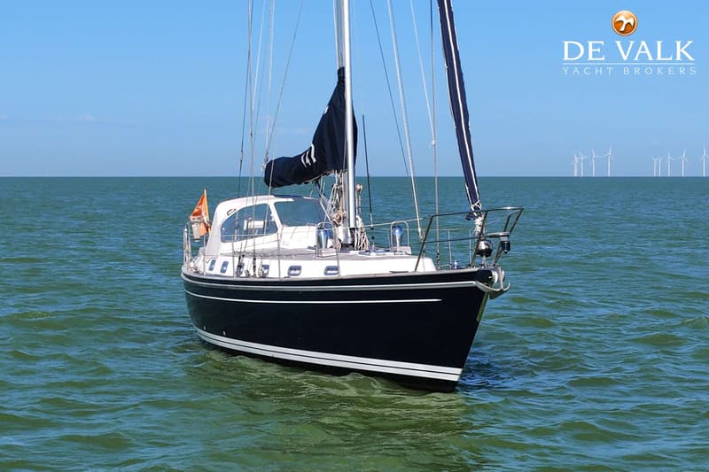 Een donkerblauwe zeilboot met witte strepen op de romp drijft op groen water onder een helderblauwe lucht.