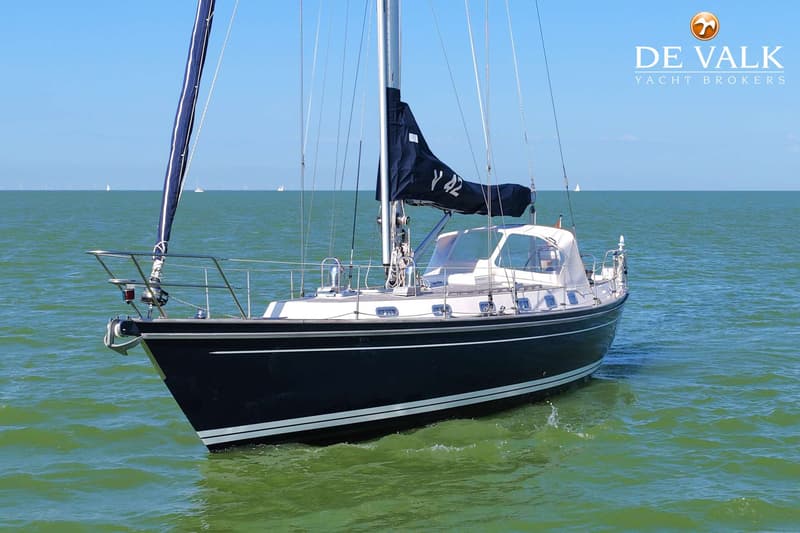 Een donkerblauwe zeilboot met witte strepen op de romp vaart op groen water onder een helderblauwe lucht.