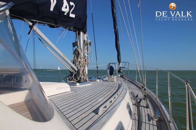 Een zeilboot met een houten dek en een donkerblauw zeil met het nummer "42" erop, vaart op open water. — Victoire 42 Classic