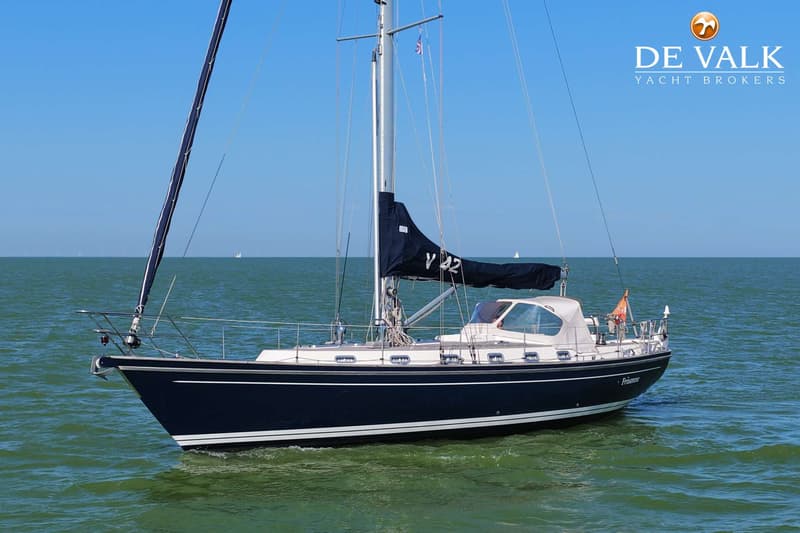 Een donkerblauwe zeilboot met een witte opbouw en een opgerold zeil ligt op het water onder een helderblauwe lucht.