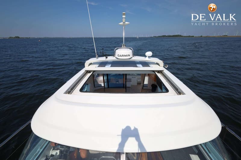 Een witte boot met een Garmin-radar en een open dak vaart op water met windmolens op de achtergrond.
