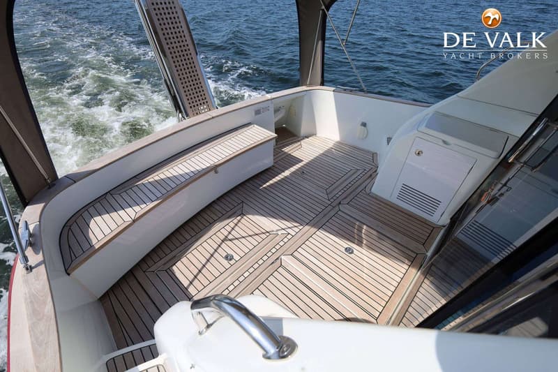 De foto toont het achterdek van een boot met een houten vloer, een bank en een trap die naar het water leidt.