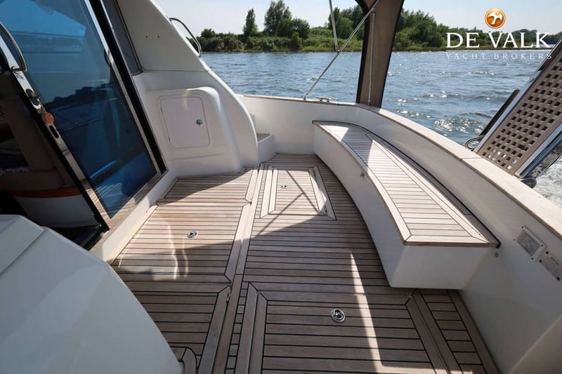 De foto toont het teakhouten dek van een boot met een bankje, een glazen schuifdeur en een zwemplateau.